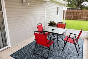 Eine Terrasse mit einem Glastisch, roten Stühlen, einem gemusterten Teppich und Blick auf eine Rasenfläche.