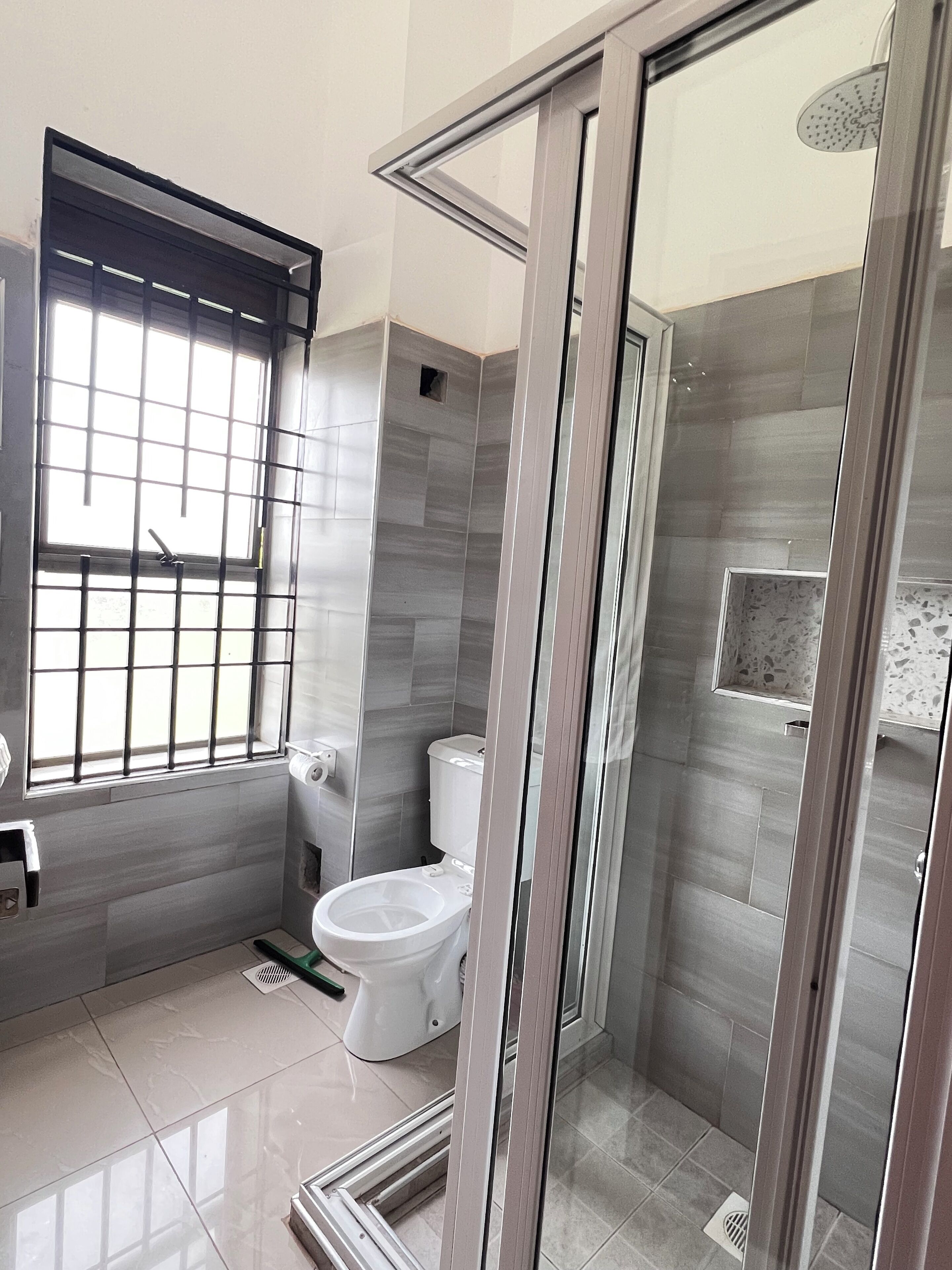 A modern bathroom with a toilet, a shower area, and a window with bars.