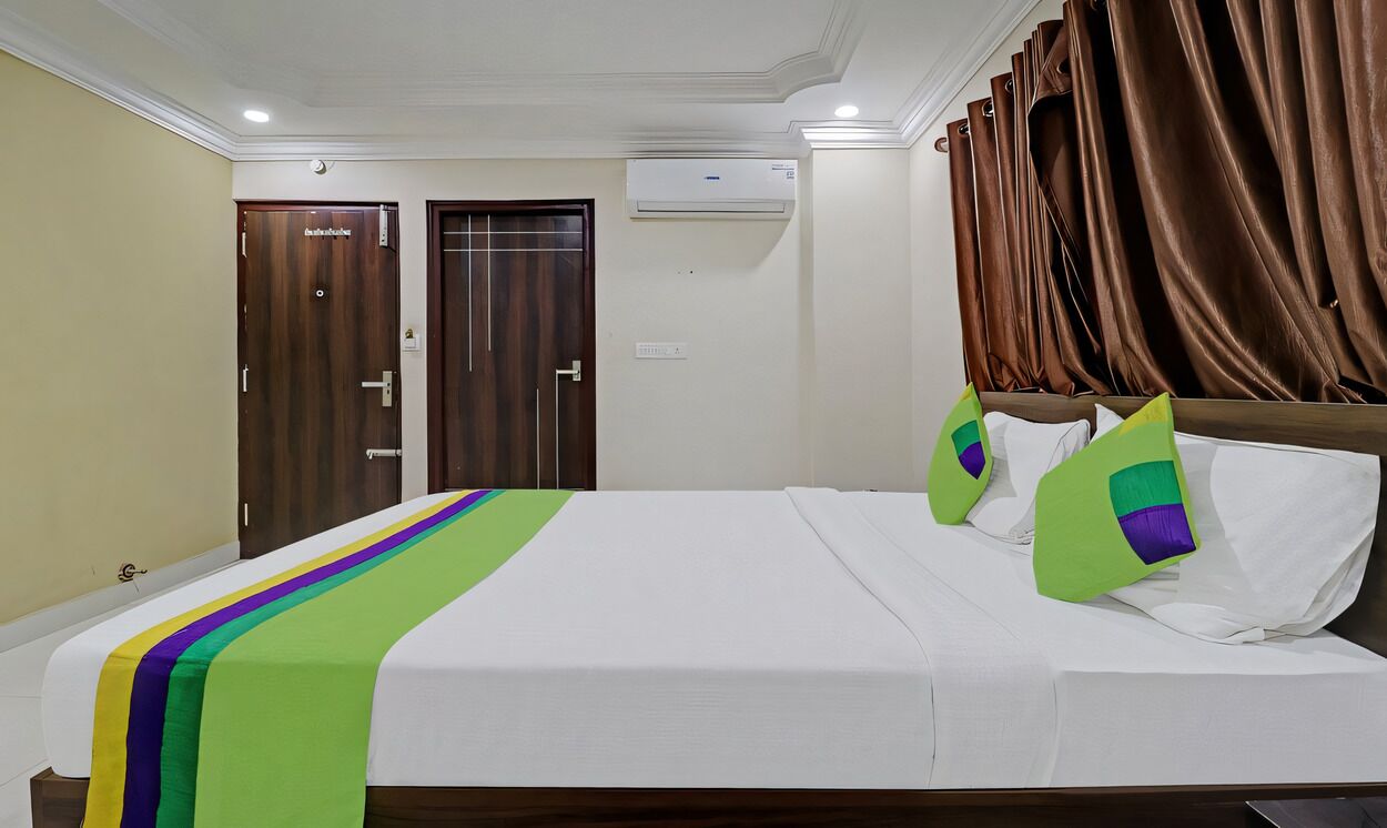 Una habitación de hotel con cama, dos puertas, un equipo de aire acondicionado y cortinas marrones.