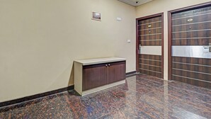 A hallway with a marble floor, a wooden cabinet, and two doors with a metal grid pattern. - Xotel Koramangala (Bengaluru)