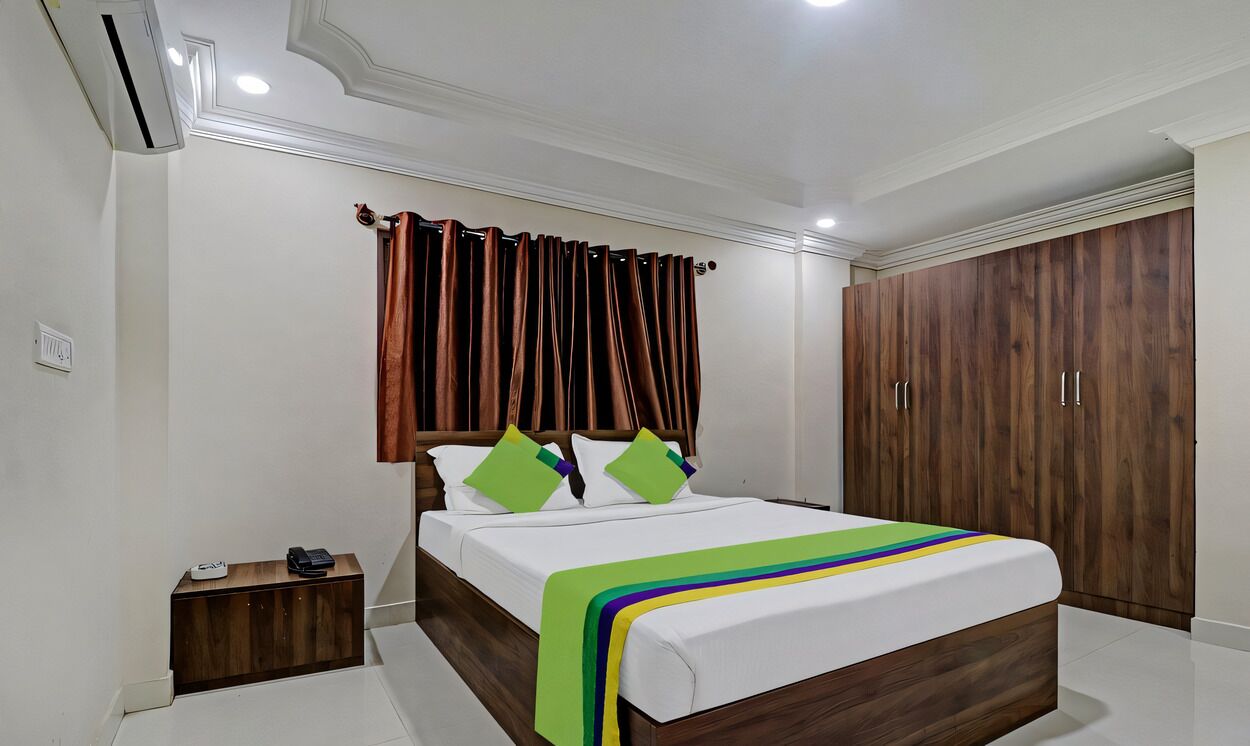 A bedroom with a wooden bed frame, white bedding, a bedside table with a lamp, and a wardrobe.