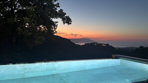 A swimming pool with a view of a sunset and a mountainous landscape.