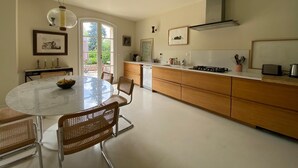 A modern kitchen with a round dining table, wooden cabinets, and a large window.