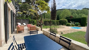 A patio with a table and chairs, a small pool, and a garden with various plants and a hedge.