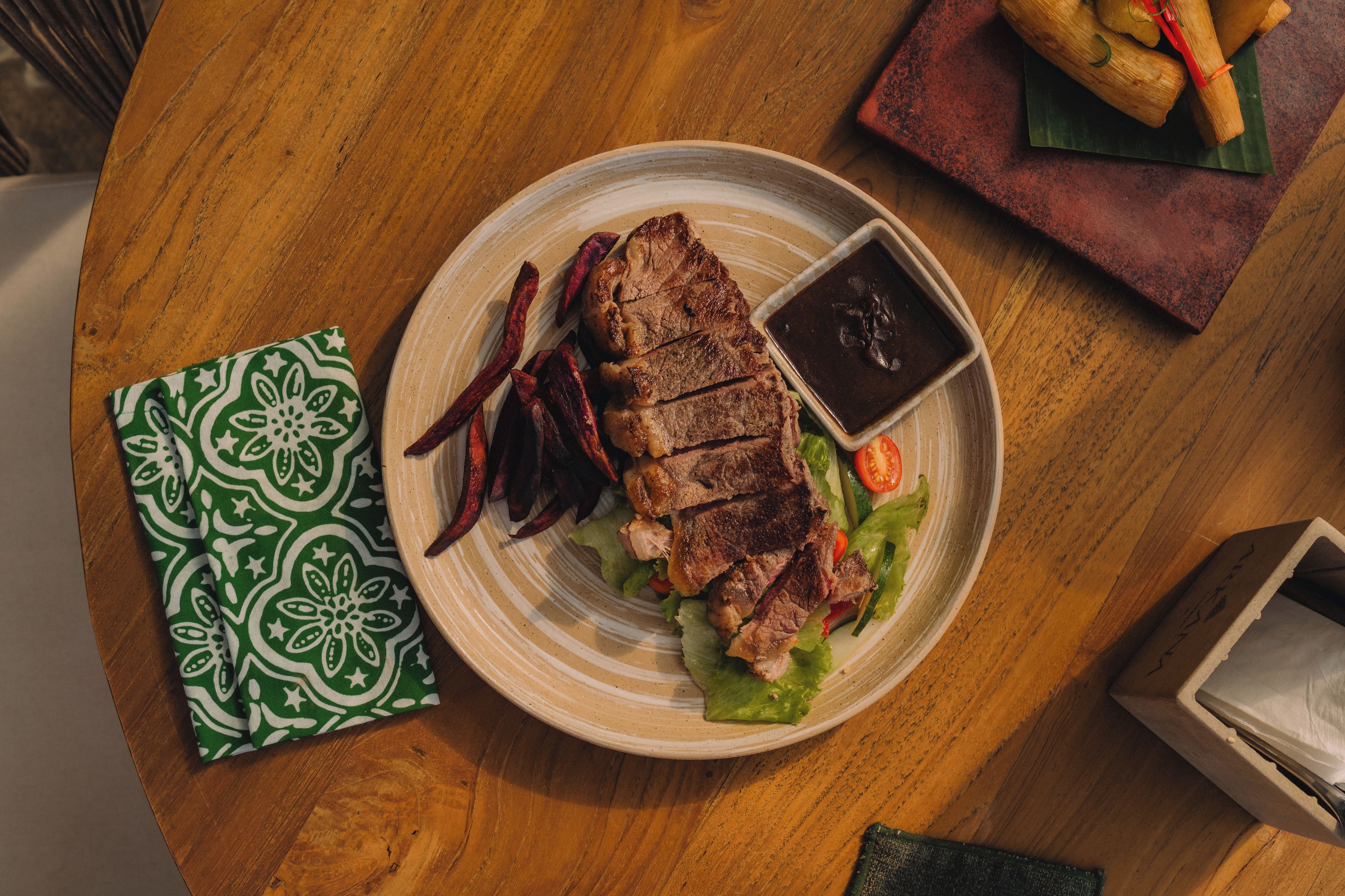 A plate with grilled meat, vegetables, and a sauce on a wooden table.