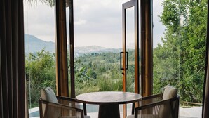 Una habitación con una mesa redonda y dos sillas, puertas de vidrio grandes, y vista a un paisaje montañoso.