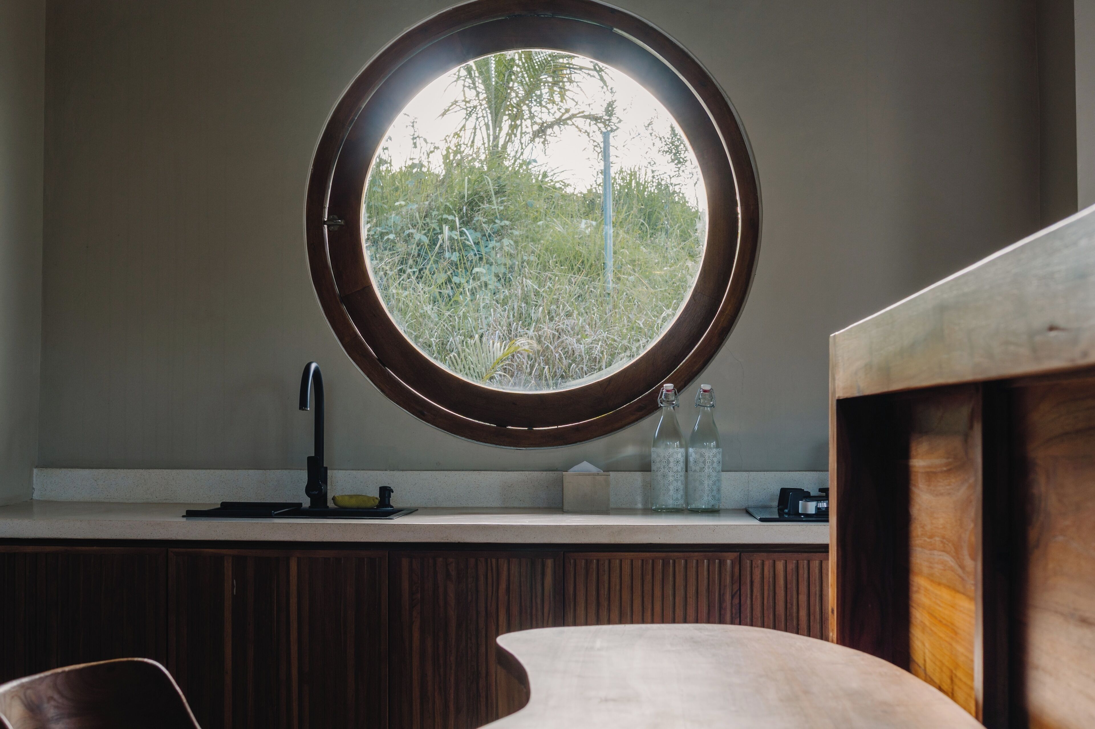 A kitchen with a round window, a sink, and a countertop with bottles.