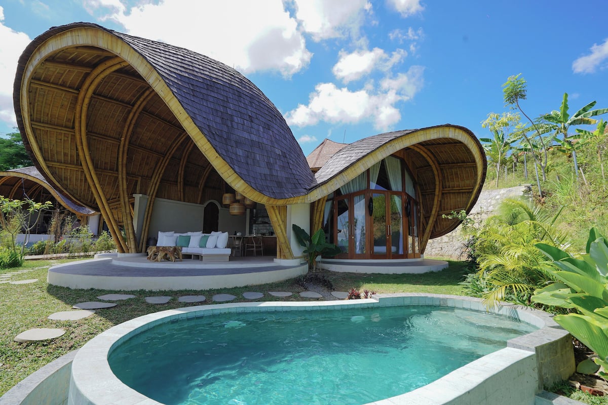 A modern house with a curved roof, a swimming pool, and lush greenery.