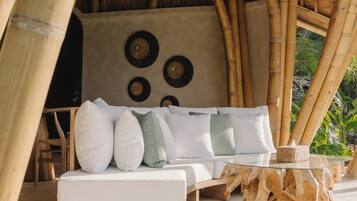 Een kamer met een bamboeframe, met een witte bank, een glazen tafel en decoratieve wandborden.