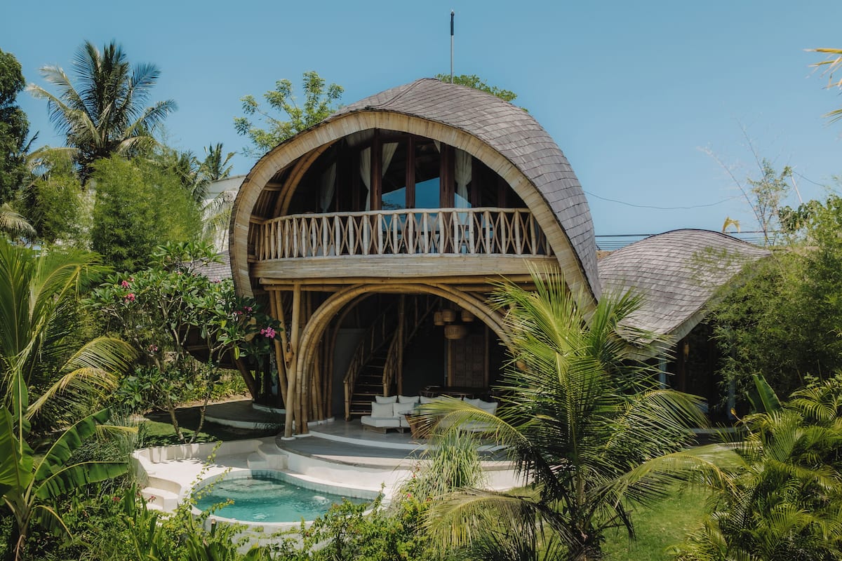 A house with a curved roof, a balcony, and a swimming pool surrounded by lush greenery.