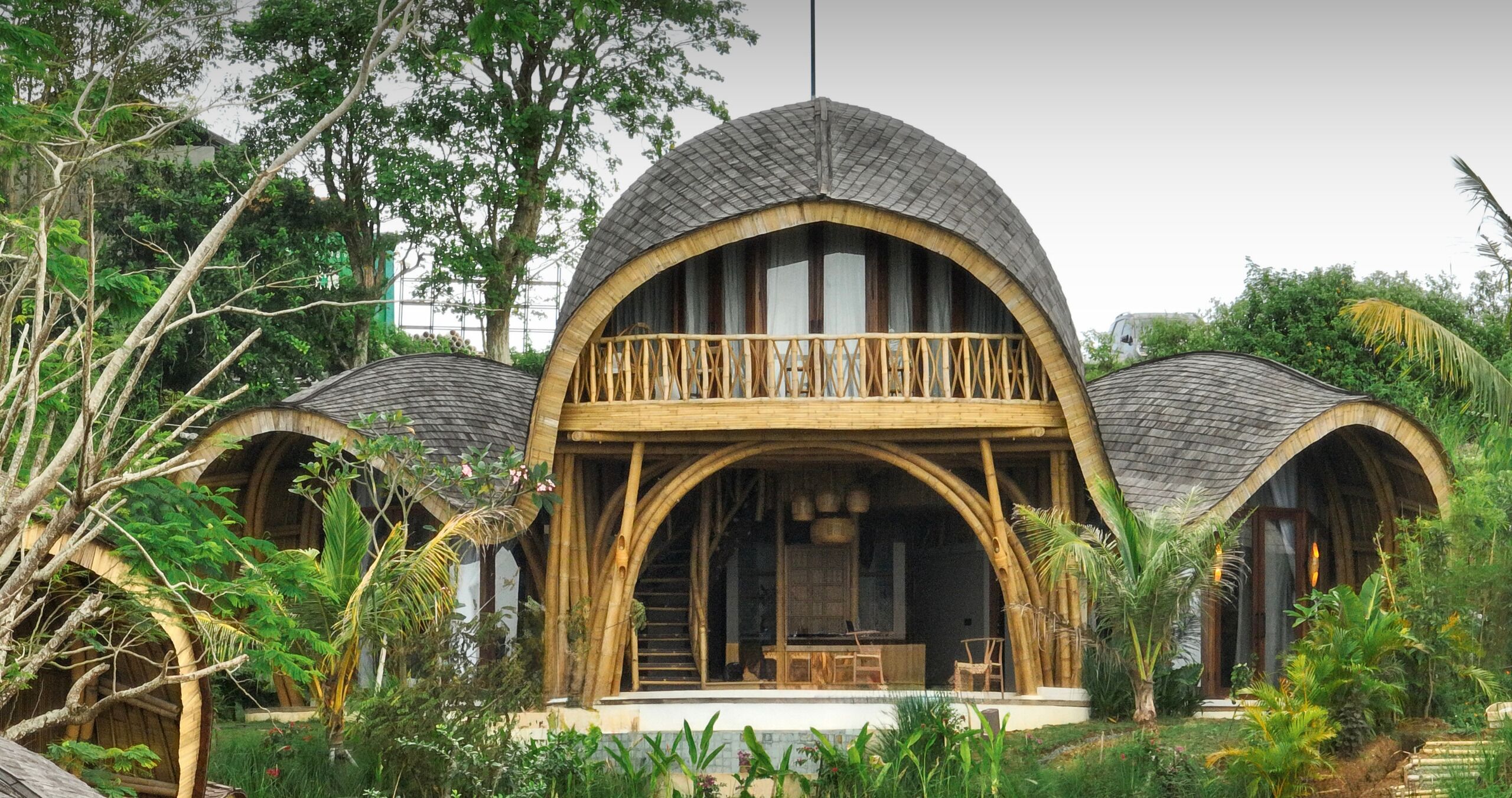 A house with a central balcony, surrounded by lush greenery.