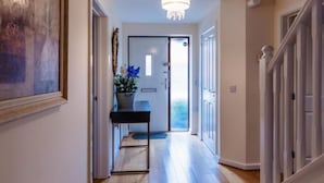 A hallway with a wooden floor, a chandelier, a door with a view, and a potted plant. - 10 Guests - 5 Bedrooms - Free Parking - Lux House (Milton Keynes)