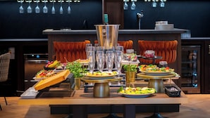 A buffet setup with various food items and drinks, a large silver serving tray, and a decorative wall with hanging lights. - Palladian Hotel (Kraków)