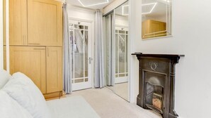 Un dormitorio con cama, armario de madera, puertas correderas de vidrio, chimenea y espejo.