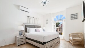 A bedroom with a bed, bedside tables, a wicker chair, and a view of the outside. - Wayaca 231 (Oranjestad)