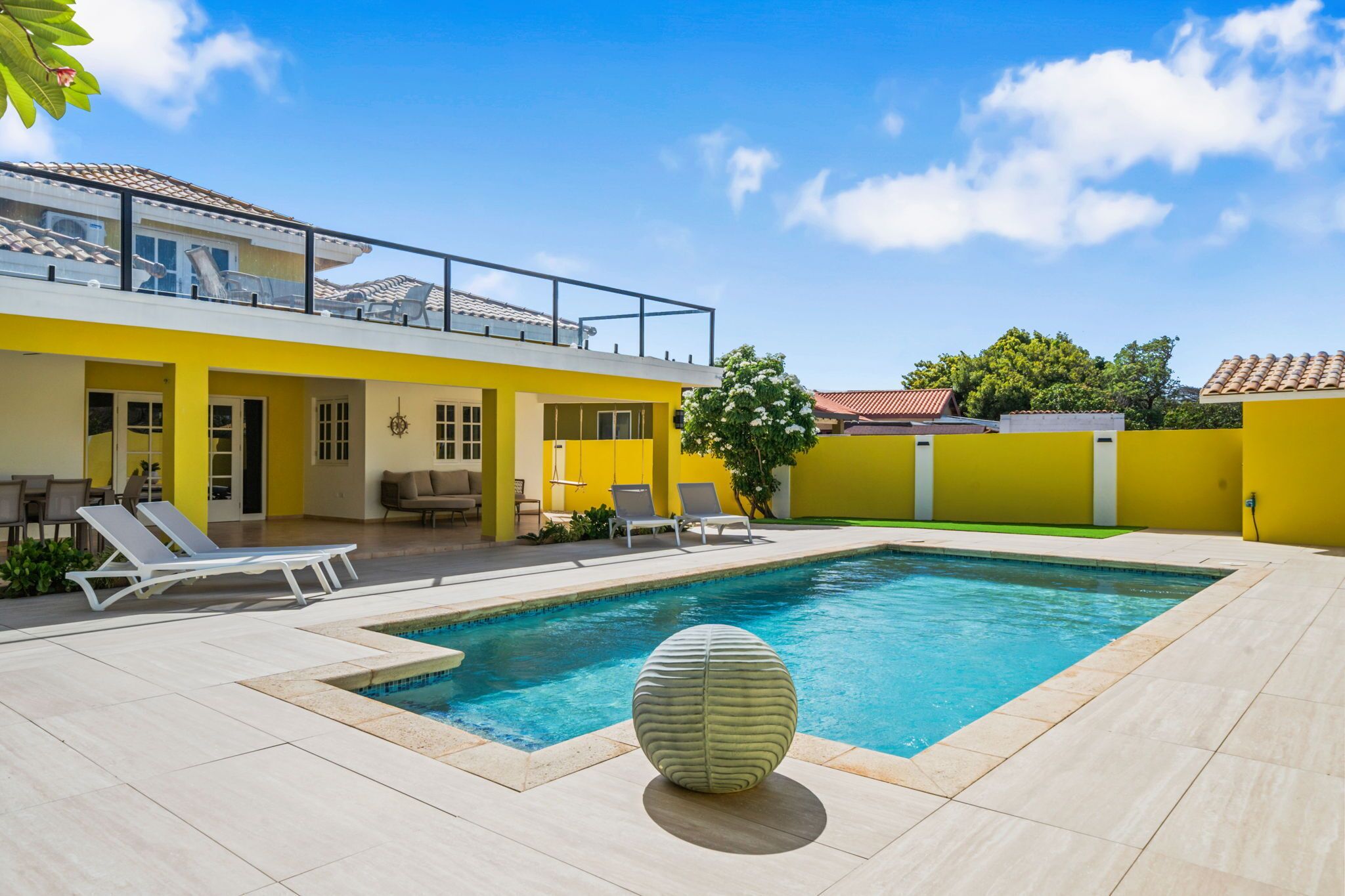 A modern yellow house with a swimming pool, outdoor seating, and a balcony.