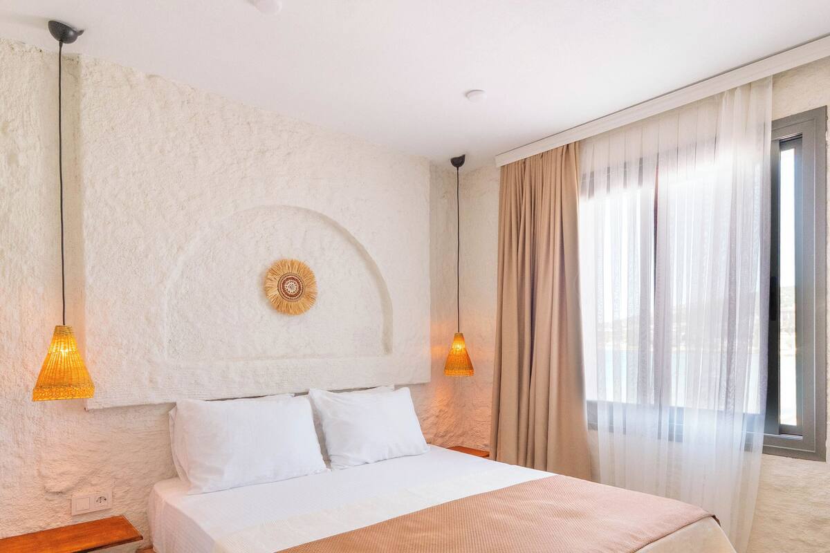 Une chambre avec un grand lit, deux lampes de chevet, un élément décoratif mural et une fenêtre avec des rideaux.