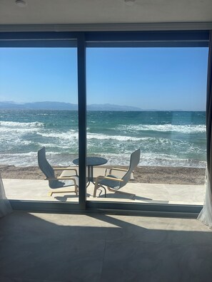 A room with a large glass door leading to a beach view. There are two chairs and a small table. - Aporte Hotel  (Çeşme)