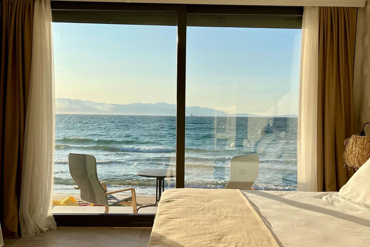 Une chambre d’hôtel avec un grand lit, une chaise et une table près de la fenêtre, donnant sur la mer.