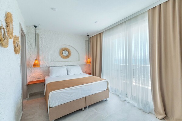 A modern bedroom with a large bed, two bedside lamps, a decorative wall piece, and sheer curtains. - Aporte Hotel (Çeşme)