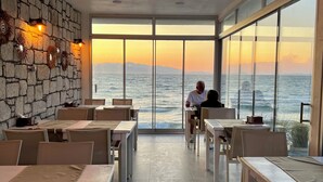 A restaurant with a stone wall and large windows overlooking the sea. Tables and chairs are arranged for dining. - Aporte Hotel  (Çeşme)