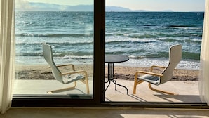 A room with a large sliding glass door leading to a beach view. Inside, there are two chairs and a small table. - Aporte Hotel  (Çeşme)