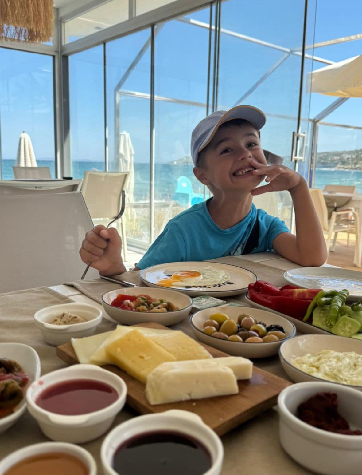 A person dining at a table with various food items and condiments, with a view of the sea through large windows.