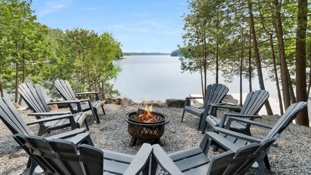 Un espacio de estar junto al lago con sillas Adirondack y un pozo de fuego.