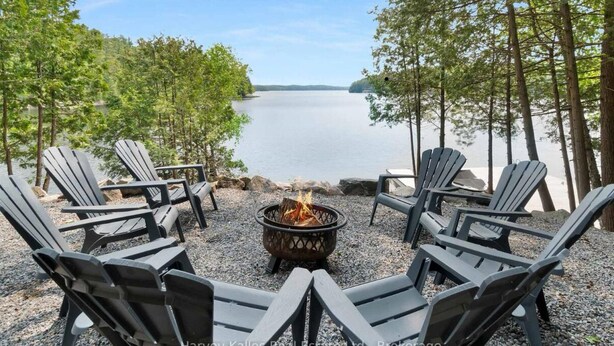 A lakeside seating area with Adirondack chairs arranged around a fire pit.