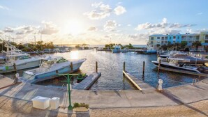 A marina with boats docked, a clear sky, and buildings in the background. - Mariners Club Unit 904, VRNR Luxury Collection, Brand New Completely Remodeled (Key Largo)