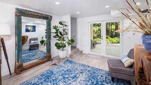 A spacious living room with a large mirror, a blue patterned rug, a gray sofa, and a potted plant. - Mariners Club Unit 904, VRNR Luxury Collection, Brand New Completely Remodeled (Key Largo)