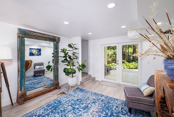 A spacious living room with a large mirror, a blue patterned rug, a gray sofa, and a potted plant. - Mariners Club Unit 904, VRNR Luxury Collection, Brand New Completely Remodeled (Key Largo)