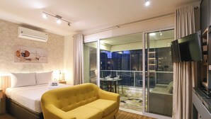 A hotel room with a bed, a yellow sofa, a TV, and a balcony with a table and chairs. - London SP Residences (Sao Paulo)