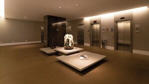 A modern lobby with a reception desk, two seating areas, and three elevators. - London SP Residences (Sao Paulo)
