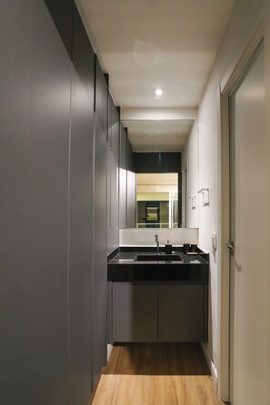 A narrow hallway leading to a kitchen with a black countertop, a sink, and cabinets. - London SP Residences (Sao Paulo)