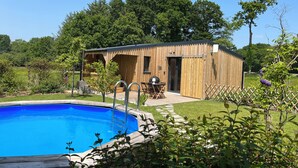 A wooden cabin with a pool, surrounded by lush greenery and trees. - Côté jardin cottage (around Dinan) (Bobital)