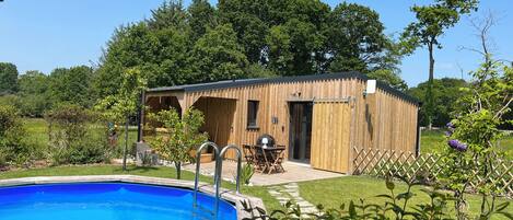 Una cabaña de madera con piscina, rodeada de abundante vegetación y árboles.