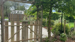 A wooden gate with a wooden pergola overhead, surrounded by a garden with stone pathways and greenery. - Côté jardin cottage (around Dinan) (Bobital)