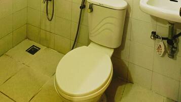 A toilet with a tank, a shower hose, and a sink.