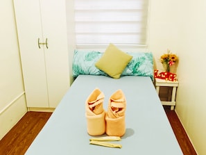 A neatly made bed with a blue sheet, a pair of shoes on the bed, and a small bedside table with a flower vase and a sign that says 'LOVE'. - Amigas Transient House (Santo Tomas)