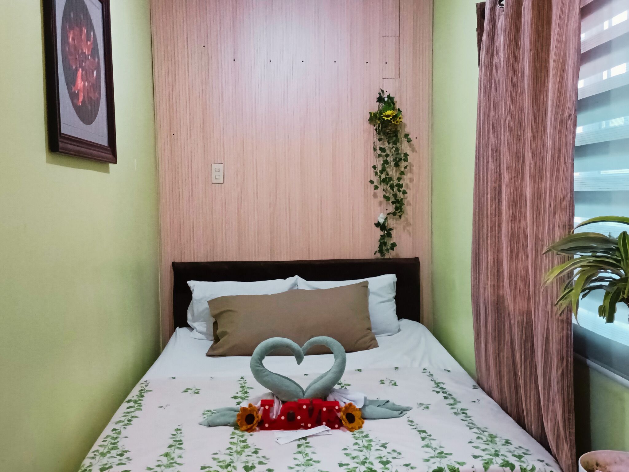 Camera da letto con un letto, cuscini, una decorazione a forma di cuore e una pianta.