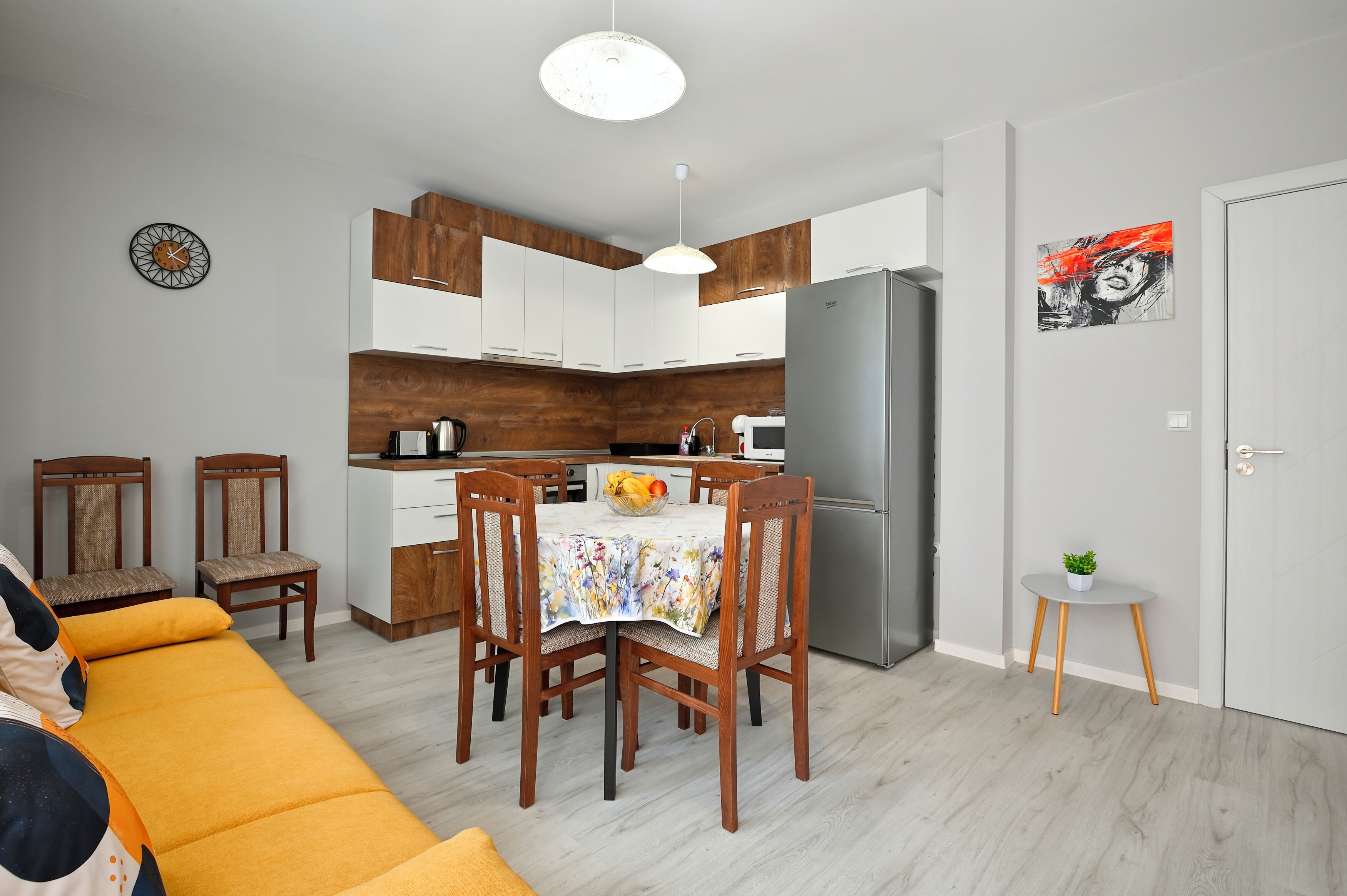 A compact kitchen with modern appliances, wooden cabinets, and a dining area with a floral tablecloth.