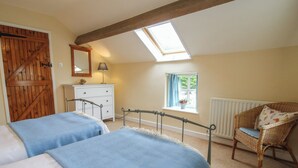 A bedroom with two beds, a wooden door, a dresser, a chair, a window, and a skylight.