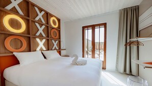 Een moderne hotelkamer met een groot bed, een houten hoofdeinde met verlichte letters, een handdoek in de vorm van een zwaan, en een transparante glazen tafel.