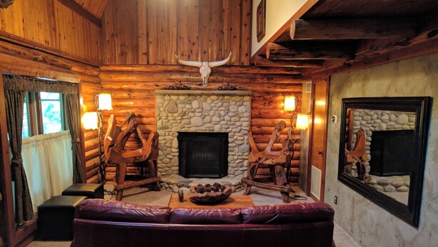 A log cabin interior with a stone fireplace, wooden furniture, and a large wooden sculpture. - Charming Cozy 2-bedroom cabin with WiFi, in enchanting Canyon Lake on the River (Canyon Lake)