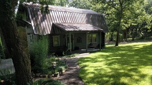 A rustic log cabin with a porch, surrounded by a well-maintained lawn and trees. - Charming Cozy 2-bedroom cabin with WiFi, in enchanting Canyon Lake on the River (Canyon Lake)