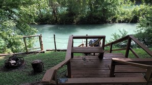 A wooden deck overlooking a calm river, surrounded by lush greenery. - Charming Cozy 2-bedroom cabin with WiFi, in enchanting Canyon Lake on the River (Canyon Lake)