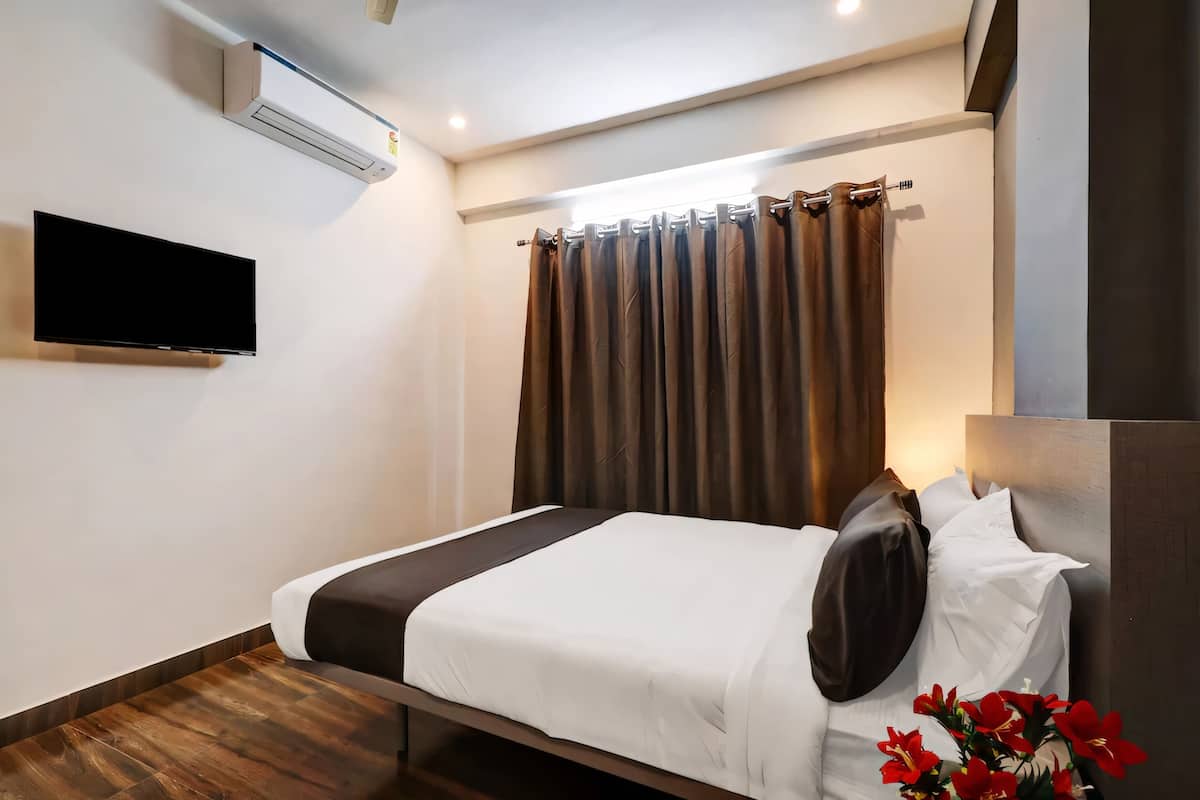 A neatly made bed with white and dark bedding, a mounted TV, and a wall-mounted air conditioner.