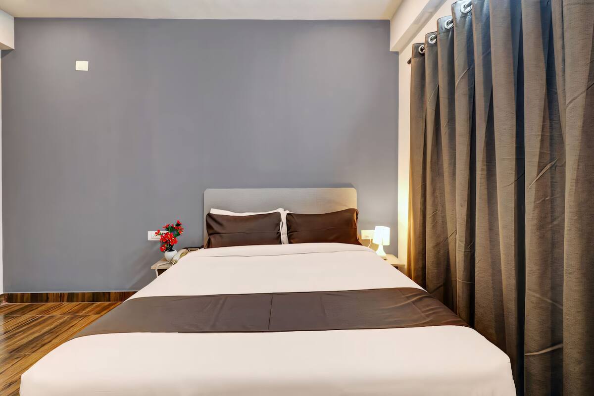 A neatly made bed with a headboard, a bedside table with a lamp, and a curtain on the window.