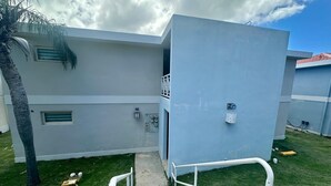 Un bâtiment moderne doté d’un escalier menant à un balcon, entouré d’une pelouse bien entretenue et d’un palmier.
